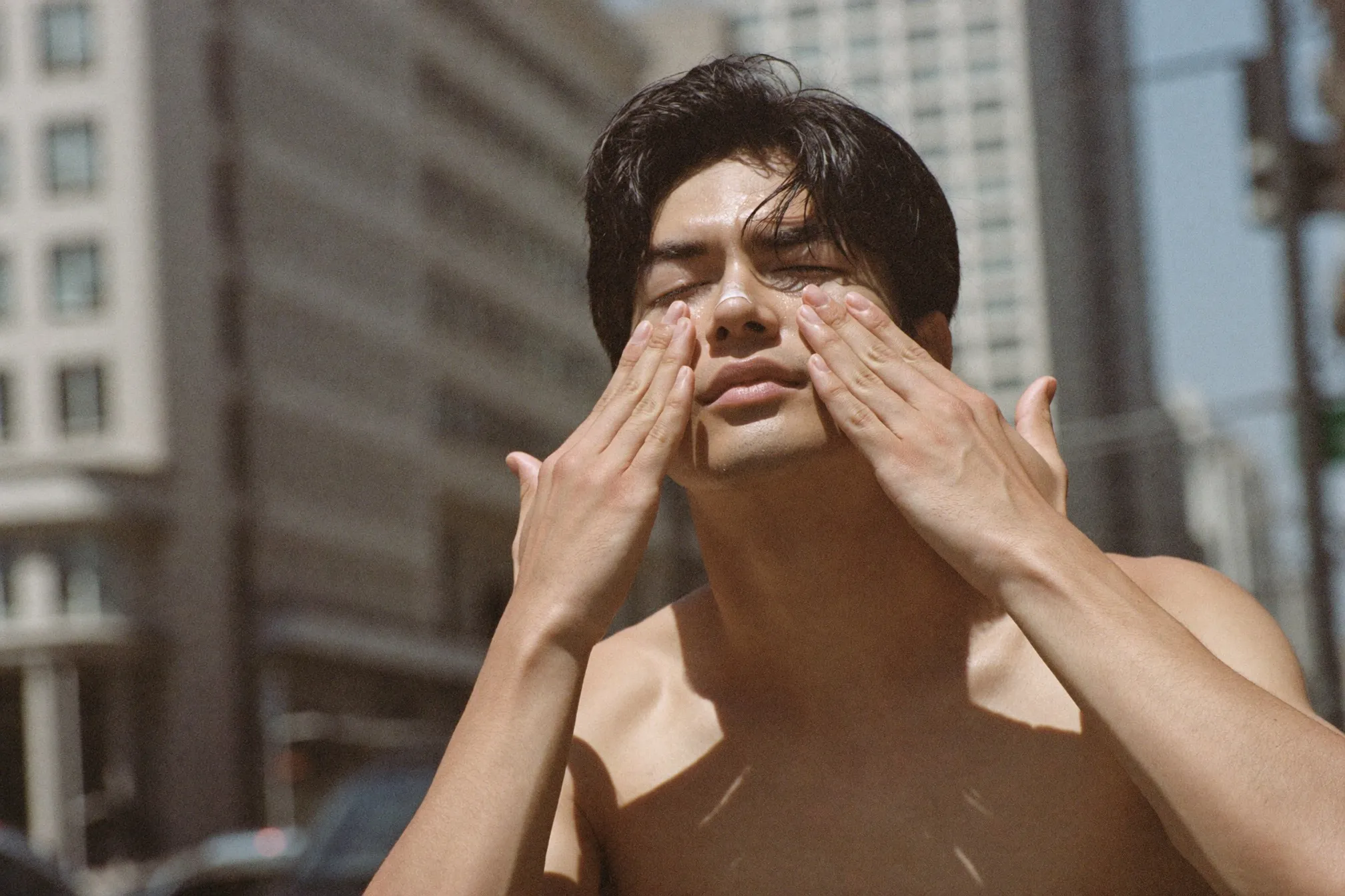 Man applying sunscreen to his face outdoors on a bright day in the city